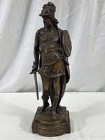 Front view of Roman gladiator bronze statue with helmet, sword, shield, and armored skirt standing on a platform