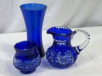 Overall lot of three cobalt blue glass items including creamer/pitcher and two vases shown side by side.