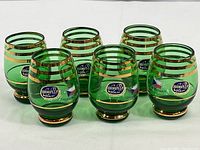 Six green cordial glasses in a group with visible labels and gold stripes