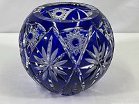 Round cobalt blue crystal bowl with intricate cut clear starburst and geometric patterns on a white background.