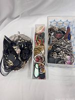 Photo showing two containers filled with mixed jewelry including black beaded necklace, bracelets, rings, watch, and earrings in various styles.