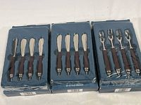 Three boxes containing the cocktail cutlery showing two sets of four spreader knives and one set of four cocktail forks, all with brown textured handles.