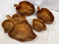 Photo of four carved Monkey Pod wood serving bowls in natural finish arranged on white surface showing leaf shapes and sizes.