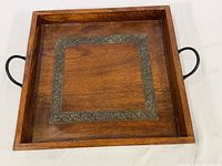 Top view of square wooden tray showing decorative metal trim inlaid in the surface and black metal handle on one side.