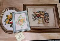 Three theorem paintings arranged on a wooden surface showing oval, small rectangular, and large rectangular frames with fruit and floral themes.