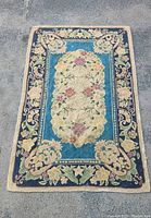 Full view of the vintage hand hook rug showing overall floral design on blue and cream background.