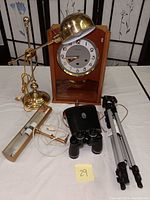 Wide view showing all lot items: clock, brass desk lamp, showcase lamp, binoculars with case, and tripod.