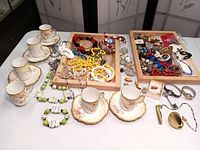 Overview of lot with costume jewelry, teacups and saucers laid out on table