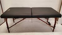 Full side view of black padded massage table open showing two cushioned sections and metal frame legs.
