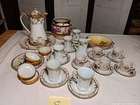 Photo showing overall collection of teapot, vase, multiple demitasse cups, saucers, creamers, small dishes, and serving bowl on table.