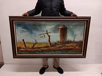 Person holding oversized framed oil painting showing rustic farm scene with silo and signpost under a moody sky.