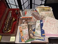 Overview of tenor saxophone in opened case alongside sheet music and calendar page
