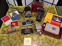 Overview of all items in lot on yellow patterned surface, showing cameras, boxes, and holiday items.