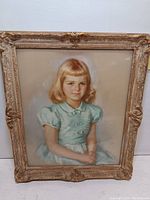 Framed pastel portrait of a young girl with blonde hair, wearing a blue dress.