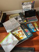 Full view of lot showing two adult colouring books, drawing pad, pastel kit, coloured pencils, mechanical pencil leads, glue stick, and cards.
