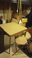 Card table with textured top and one folding chair in a basement setting.