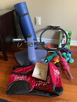 Overview of the exercise equipment lot including hand weights, muscle rollers, Pilates ring and mat, mini seated cycle, resistance bands, posture medic, yoga DVD, and gym bag.