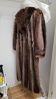 Full length view of the raccoon fur coat hanging on rack showing the length reaching near floor and rich brown fur with natural color variation.