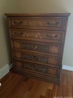 Front view of the five drawer chest showing carved drawer fronts and brass handles.