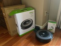 iRobot Roomba e6 robot vacuum with original packaging boxes and replenishment kit box on hardwood floor.