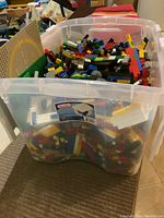 Clear Sterilite storage tote filled with Lego blocks and baseplates, showing large volume of assorted bricks in various colors and sizes.