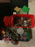 Top-down view of a large red bin filled with assorted Lego parts including windows and wheels, surrounded by baseplates and a pirate ship set.