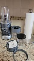 Nutribullet blender with 2 large vessels, 1 small vessel, lids and paper towel holder on kitchen counter