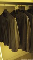 Two brown men's leather jackets hanging on hangers in a closet. Jackets appear lightly used with a classic leather texture.