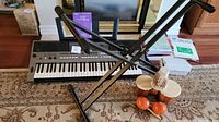 Full lot overview showing digital keyboard on X stand with foot pedal, maracas, and bongo drums placed nearby, plus books stacked behind keyboard.