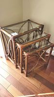 Three nesting tables with bamboo frames and glass tops stacked together showing full set and size graduation.