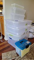 Stacked clear plastic storage bins of varying sizes, including a Sterilite bin and a plastic file tote with blue lid