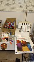 Kenmore serger with various sewing accessories on table including threads, needles, and books.