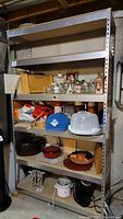 Full view of metal frame shelving unit with composite wood shelves loaded with various household items (not included in lot).