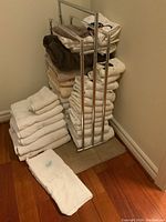 Full view showing a large stack of white and beige bath towels, including some brown towels, stacked on and around a chrome and acrylic towel rack.