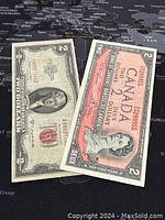 Two banknotes displayed on a map surface, US $1 Federal Reserve Note with red seal and Canada $2 banknote in coral red.