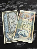 Two Canadian 5 dollar bills from 1954 and 1972 placed on a black and white map background