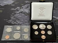 1977 coin set sealed in a transparent plastic holder alongside 1987 coin set displayed in black Royal Canadian Mint case