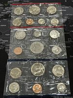 Three plastic-sealed coin sets featuring US and Canadian coins with proof-like surfaces, showing multiple denominations.