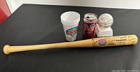 Lot overview showing signed baseball bat, signed baseball in case, two promotional cups, and commemorative Coca-Cola can on black background.