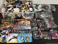 Main overview shot showing large plastic bin of mixed bricks, multiple sealed numbered polybags, instruction manuals laid out, and several small resealable bags.