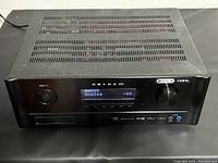 Front-angled view of black metal chassis powered on, showing perforated top panel, display and controls