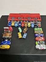 Lot of assorted Disney Pixar Cars diecast vehicles arranged with red fire station starting gate accessory in background