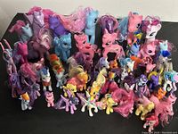 Front view of over 40 My Little Pony figurines displayed together showing various colors and styles of manes and tails. Figures arranged on black background surface.