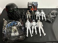 All items laid out on a black surface showing helmets, action figures, glass set and folder.