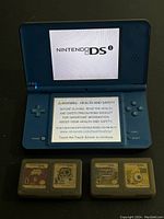 Open Nintendo DSi powered on to splash and health/safety screens, console and four game cartridges below