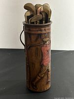 Cylindrical tin container with woodgrain print, wire handle, embossed club heads visible at top