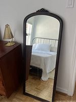 Full length view of the vintage dark wood wall mirror leaning against the wall showing the entire mirror including the carved detail at the top, the reflective glass, and part of the surrounding room environment.