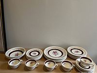 Photo showing full set of porcelain dinnerware including cereal bowls, dinner plates, tea cups, saucers, bread and butter plates, and salad/lunch plates with rope edge, 22K gold filigree, maroon band and floral rose point design.