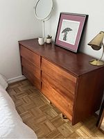Front-side angle of wooden dresser showing six drawers and brass-colored feet