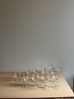 Front view showing all 11 mixed glasses arranged on a wooden surface against a plain wall, illustrating size and shape variety.